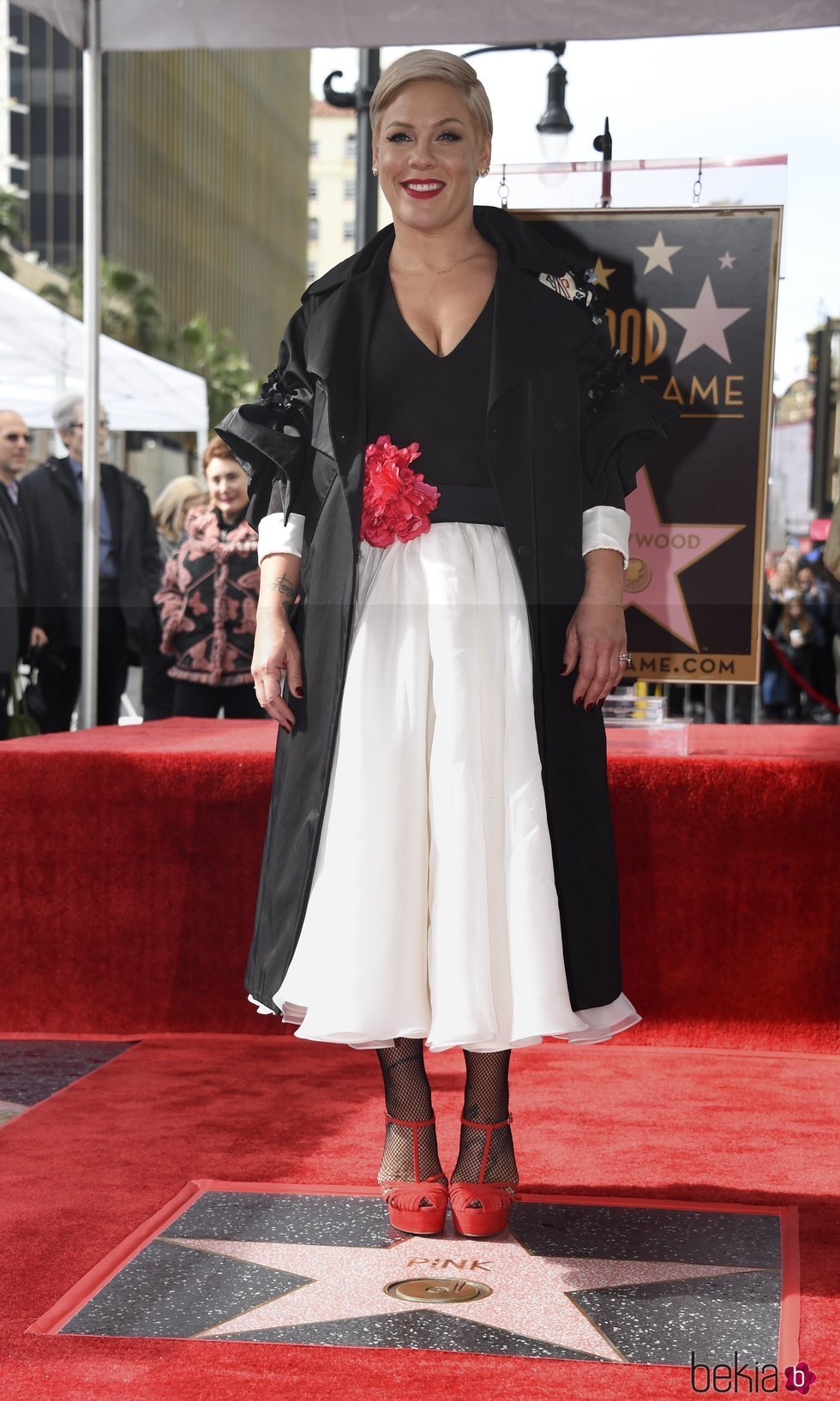 Pink con un vestido bicolor bajo un abrigo largo de mangas abullonadas y un roja en el cinturón recibiendo la estrella en el Paseo de la Fama de Hollywood
