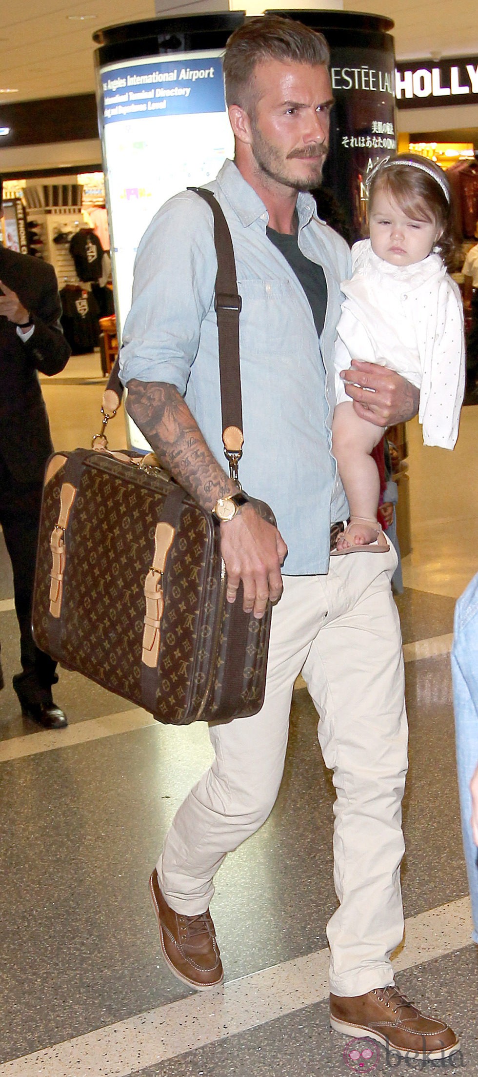 David Beckham con un pantalón de color crema, camisa azul y cartera de Louis Vuitton