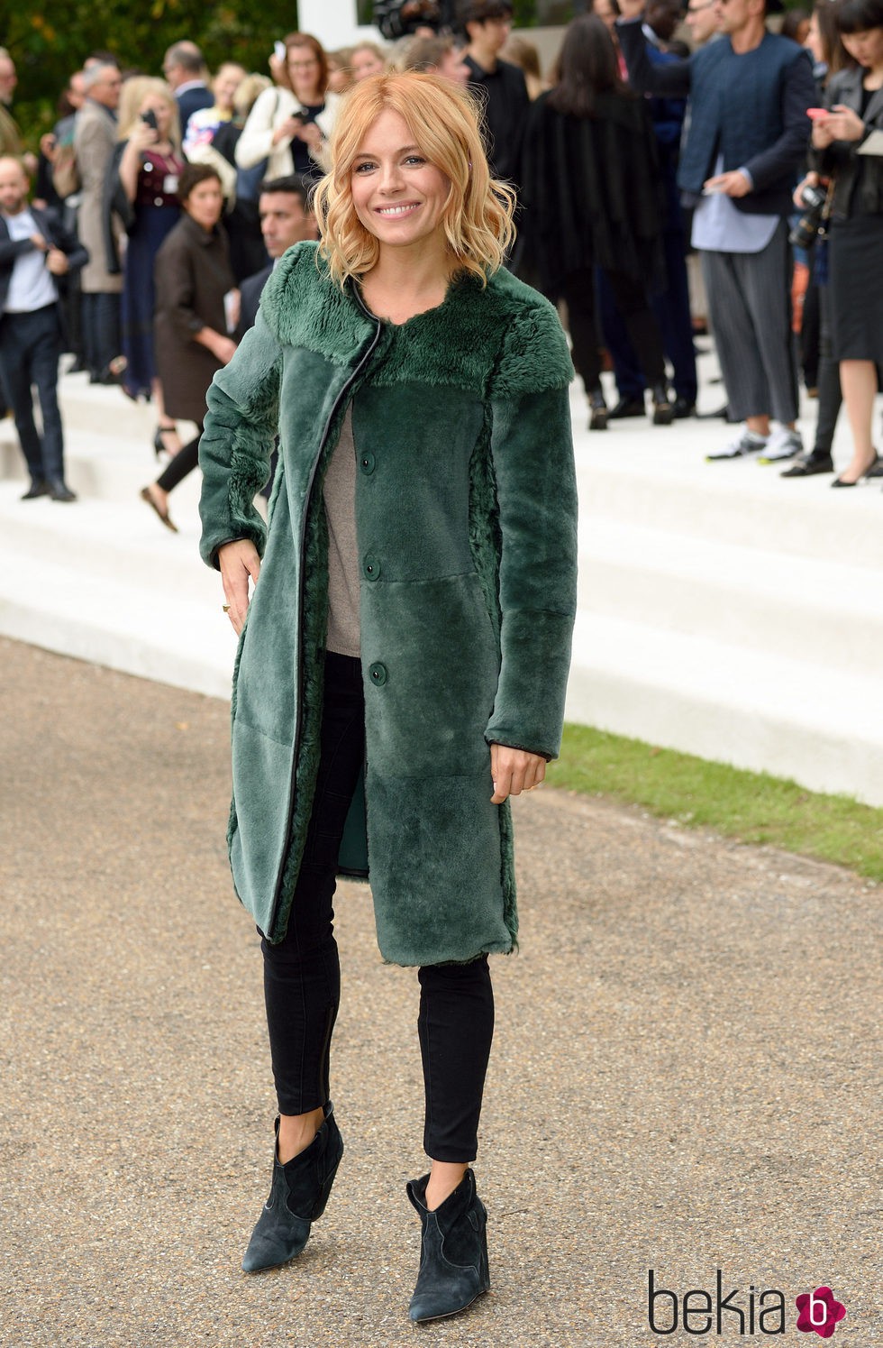 Sienna Miller con abrigo verde y pantalón pitillo negro en el desfile de Burberry en la London Fashion Week