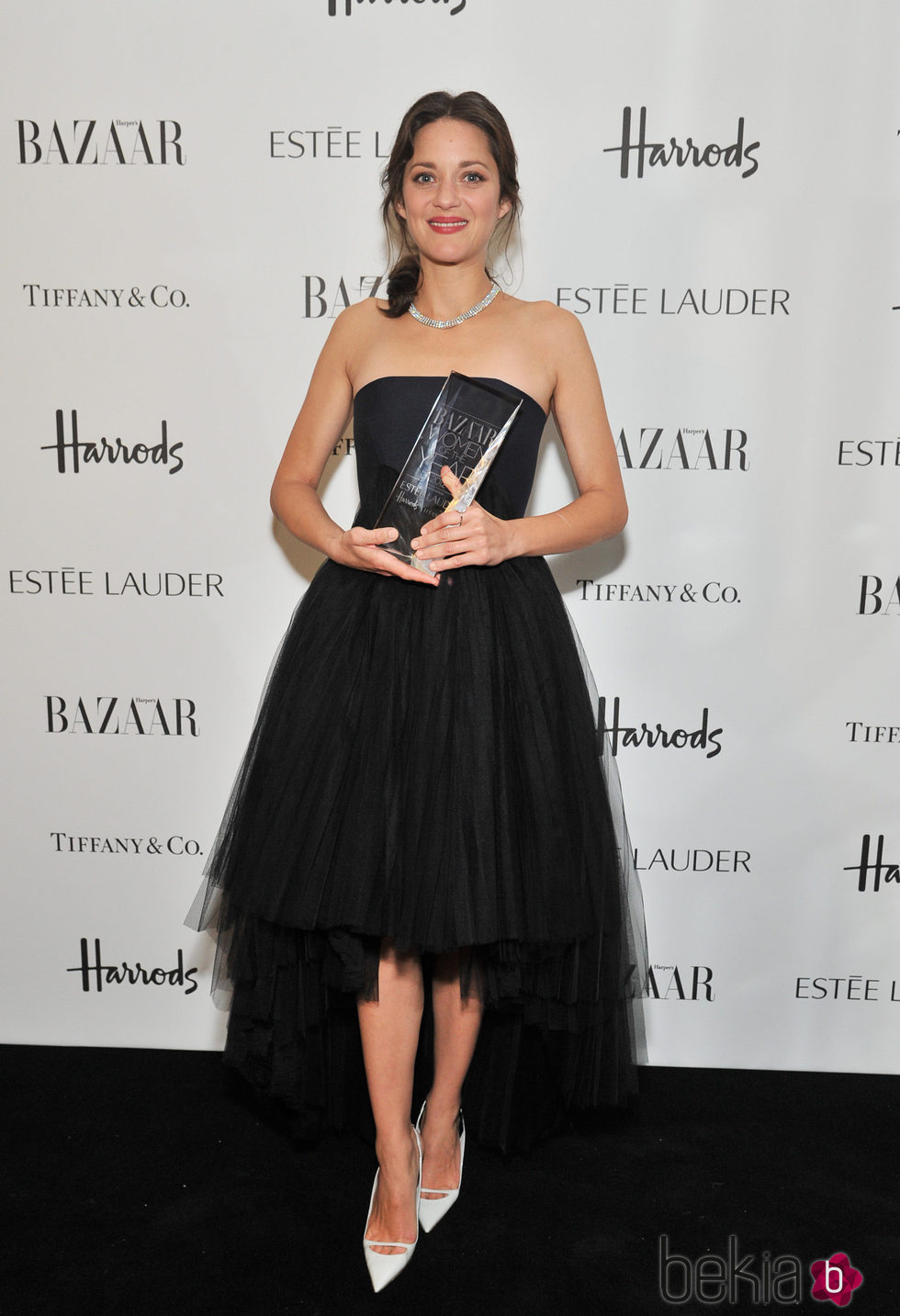 Marion Cotillard con vestido negro sujetando premio a la mujer del año de Harper