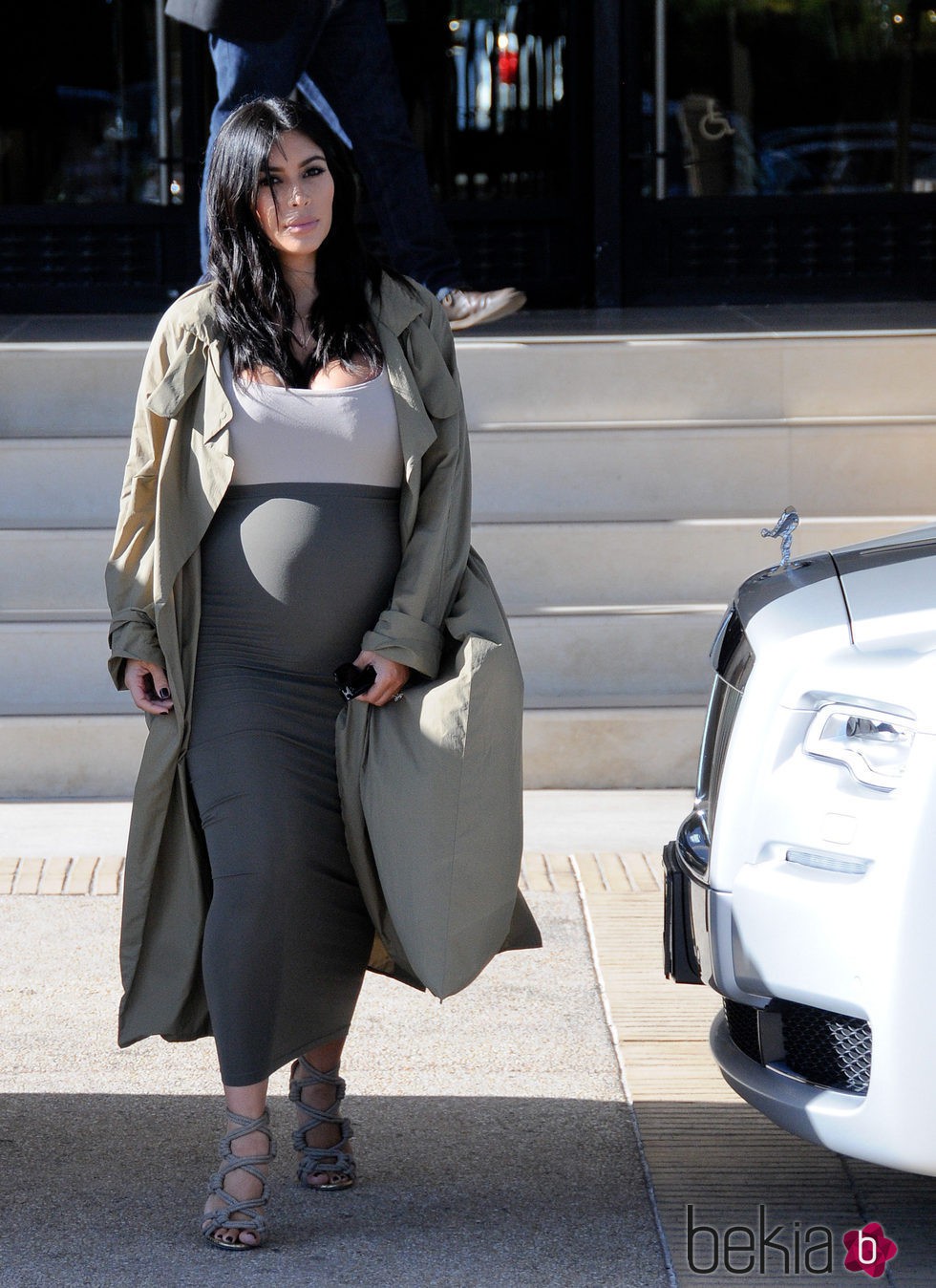 Kim Kardashian con vestido blanco y gris y gabardina larga en su segundo embarazo
