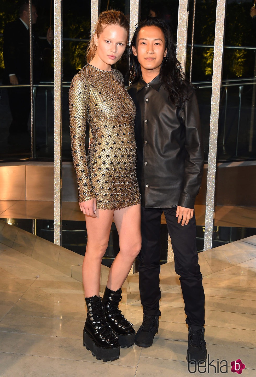 Anna Ewer junto a Alexander Wang con mini vestido ajustado en dorado y botas militares negras